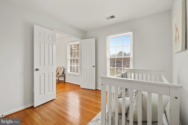 bedroom with light wood-type flooring, a nursery area, baseboards, and visible vents