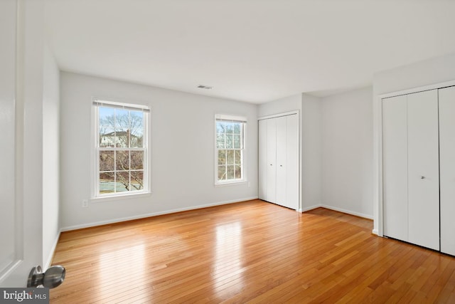 unfurnished bedroom with multiple closets, light wood-type flooring, visible vents, and baseboards