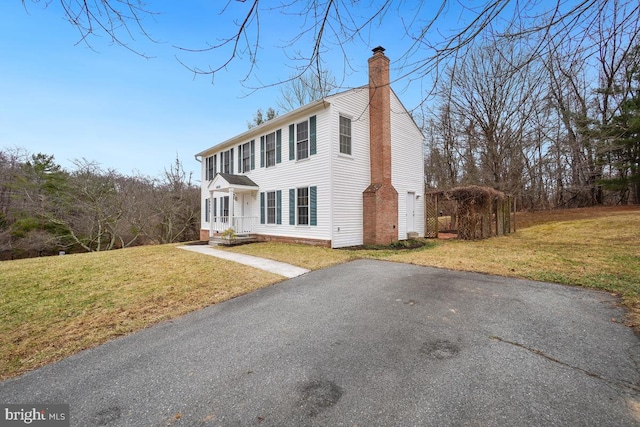 view of front facade featuring driveway, a chimney, and a front yard