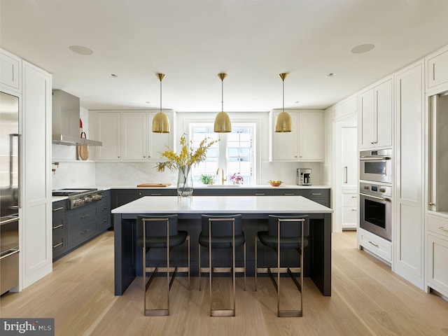 kitchen featuring a kitchen breakfast bar, wall chimney exhaust hood, light countertops, and stainless steel appliances