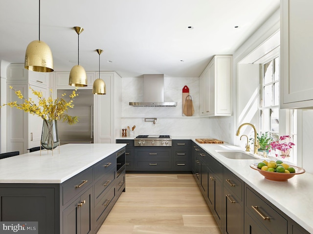 kitchen featuring decorative backsplash, wall chimney exhaust hood, built in appliances, light countertops, and a sink