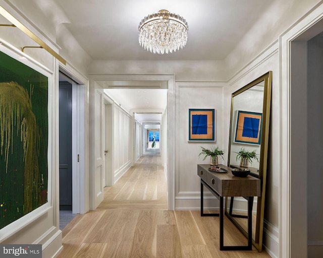 hallway featuring light wood-type flooring, an inviting chandelier, and baseboards