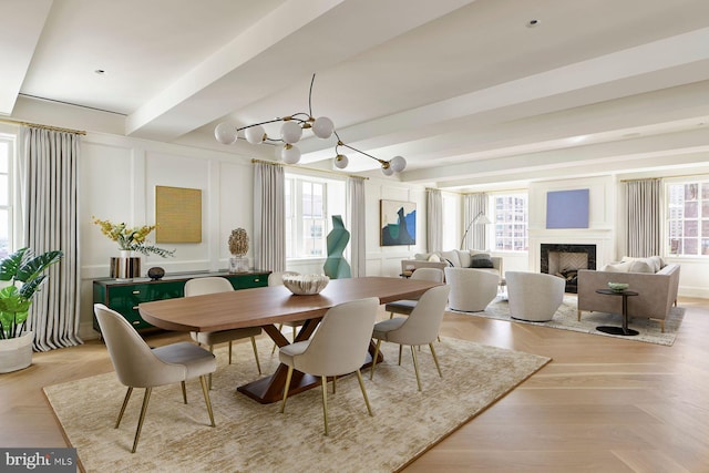 dining room with a notable chandelier, a fireplace, a decorative wall, and beam ceiling