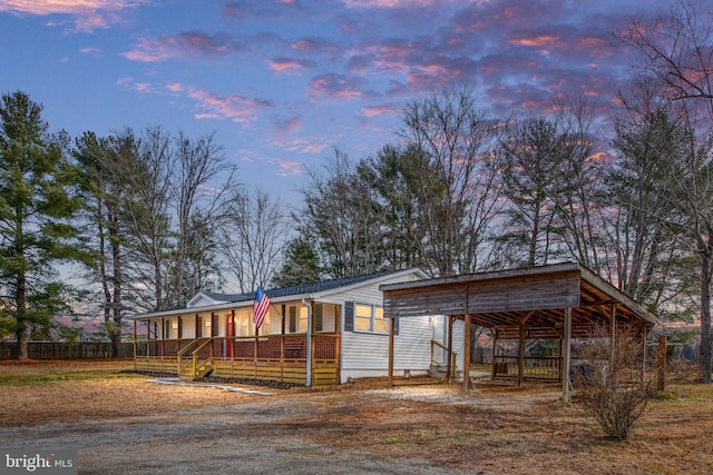 view of front of property featuring covered porch, dirt driveway, and a carport