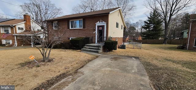 split foyer home with a front yard, brick siding, fence, and central AC