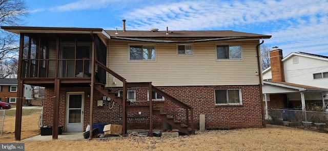 rear view of house featuring brick siding, fence, and a sunroom