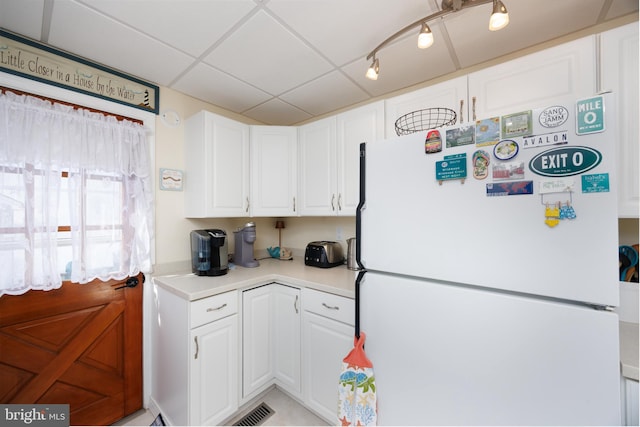 kitchen featuring light countertops, a paneled ceiling, freestanding refrigerator, and white cabinetry