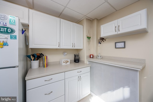 kitchen featuring light countertops, a paneled ceiling, freestanding refrigerator, and white cabinets