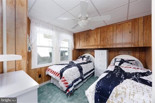 carpeted bedroom featuring a ceiling fan, a drop ceiling, and wood walls