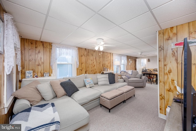 living room featuring carpet floors, ceiling fan, wooden walls, and a drop ceiling