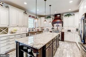 kitchen with white cabinetry, custom exhaust hood, and decorative light fixtures