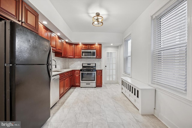 kitchen featuring baseboards, decorative backsplash, light stone countertops, stainless steel appliances, and a sink