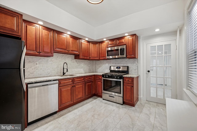 kitchen with light stone counters, stainless steel appliances, recessed lighting, backsplash, and a sink