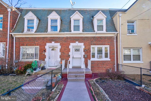 view of front facade featuring brick siding, fence, and mansard roof