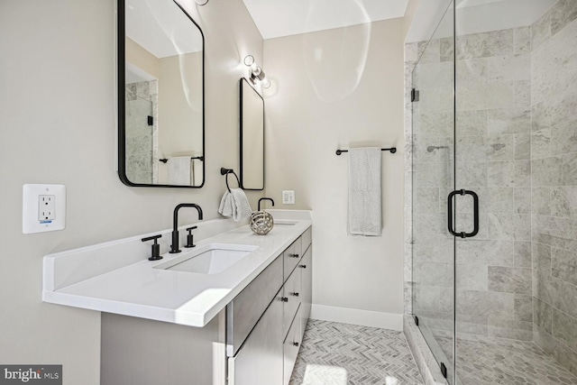 bathroom with double vanity, a shower stall, baseboards, and a sink