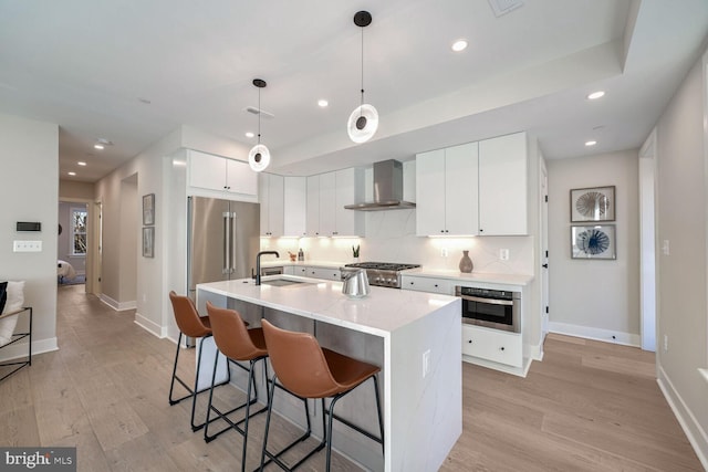 kitchen featuring a breakfast bar, a sink, appliances with stainless steel finishes, decorative backsplash, and wall chimney exhaust hood