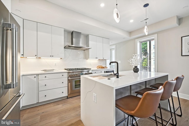 kitchen with a sink, wall chimney range hood, light wood finished floors, and high quality appliances