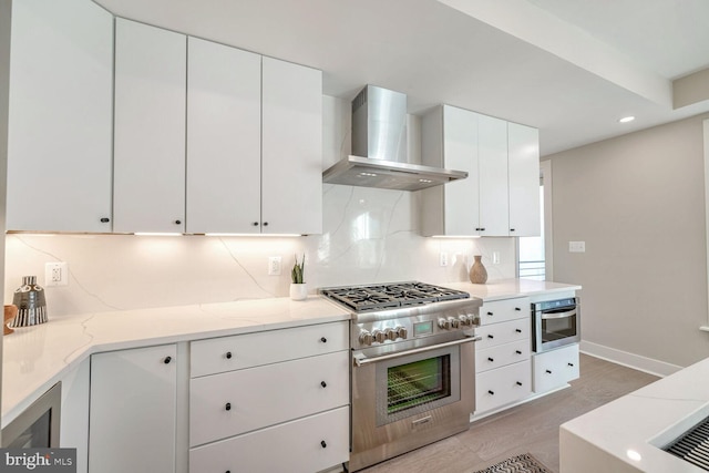 kitchen featuring stainless steel appliances, backsplash, white cabinets, light stone countertops, and wall chimney exhaust hood