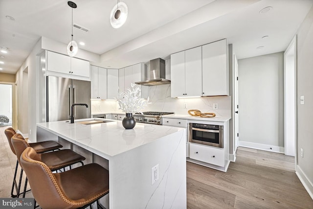 kitchen with light wood-style flooring, a sink, wall chimney range hood, appliances with stainless steel finishes, and backsplash