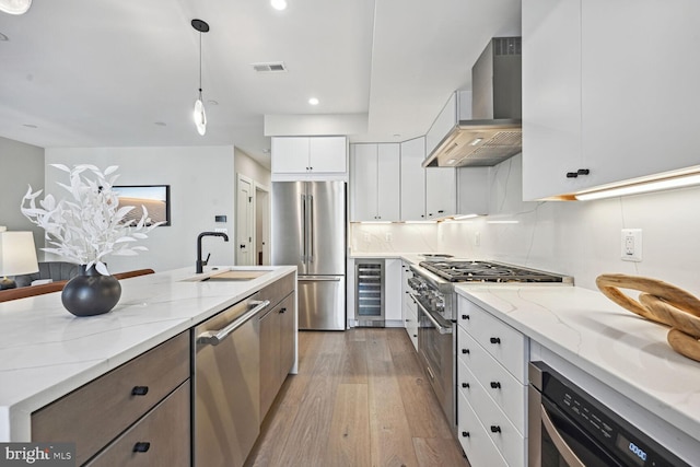 kitchen with premium appliances, wine cooler, visible vents, a sink, and wall chimney range hood