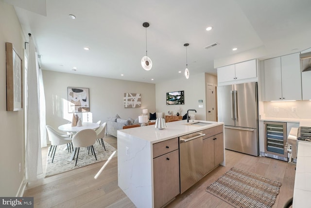 kitchen featuring stainless steel appliances, visible vents, light wood-style floors, a sink, and beverage cooler