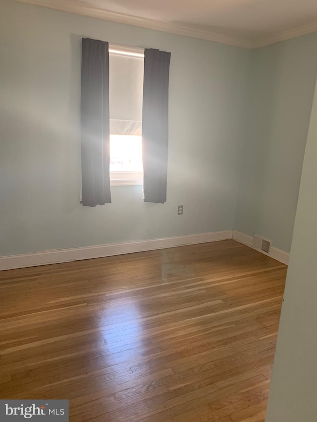 unfurnished room featuring baseboards, visible vents, wood finished floors, and ornamental molding