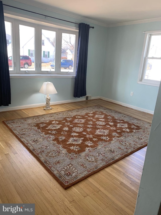 empty room featuring baseboards, wood-type flooring, visible vents, and crown molding