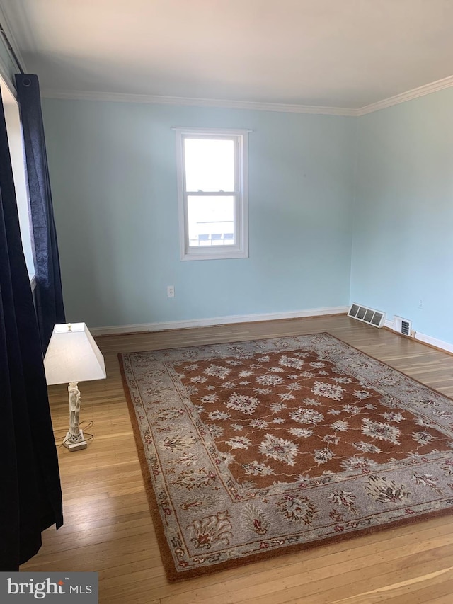 spare room featuring baseboards, visible vents, wood finished floors, and ornamental molding