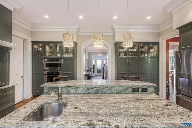 kitchen featuring light stone counters, arched walkways, stainless steel appliances, a sink, and green cabinetry