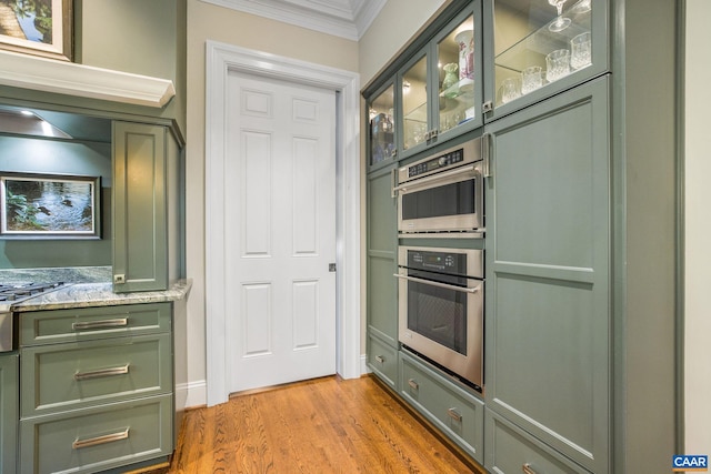 kitchen with ornamental molding, light stone counters, light wood-style floors, double oven, and green cabinets