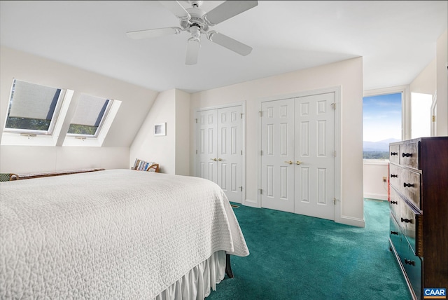 bedroom featuring two closets, dark carpet, lofted ceiling with skylight, a ceiling fan, and baseboards