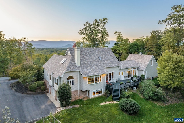 back of house with a deck, a yard, driveway, stairway, and a chimney