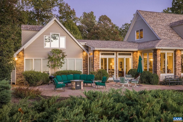 rear view of property with stone siding, a shingled roof, a patio, and an outdoor living space with a fire pit