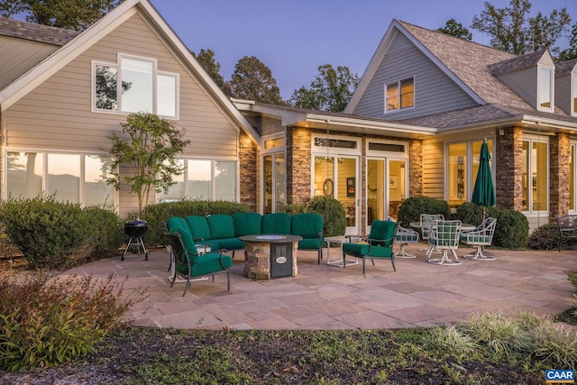 rear view of house with an outdoor living space with a fire pit, stone siding, and a patio area