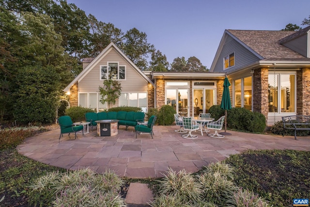 back of property featuring stone siding, a patio area, and an outdoor living space with a fire pit