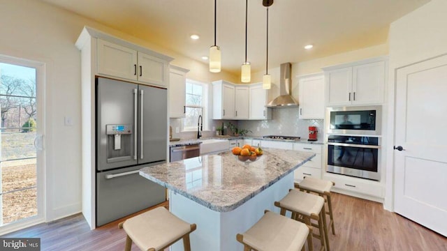 kitchen featuring a kitchen island, appliances with stainless steel finishes, a breakfast bar area, decorative light fixtures, and wall chimney range hood