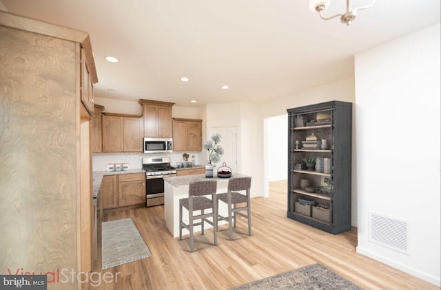kitchen with visible vents, a kitchen island, appliances with stainless steel finishes, brown cabinets, and light wood-style floors