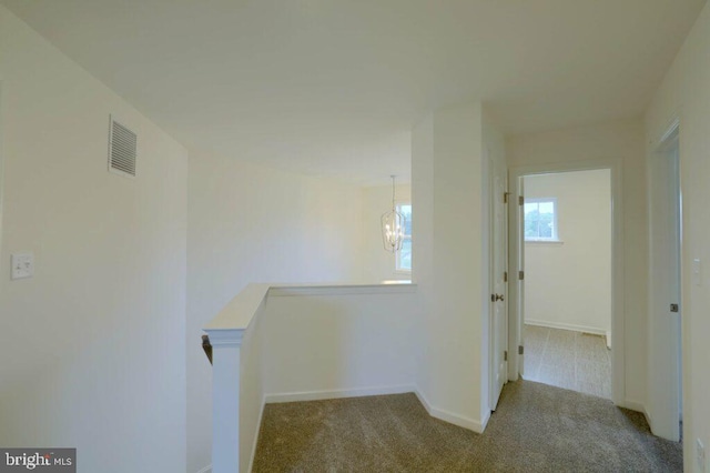 corridor with light colored carpet, visible vents, baseboards, an upstairs landing, and an inviting chandelier