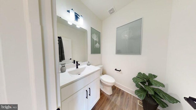half bathroom featuring visible vents, wood finished floors, vanity, and toilet
