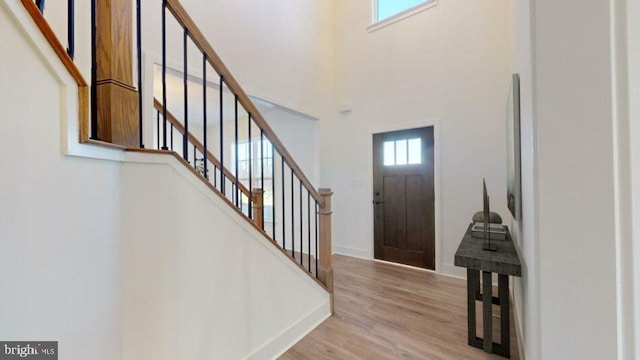 entryway featuring stairs, light wood-type flooring, a towering ceiling, and baseboards