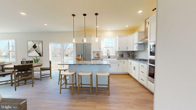 kitchen featuring pendant lighting, stainless steel appliances, white cabinetry, a kitchen island, and light wood-type flooring