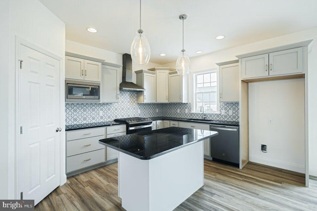 kitchen with a kitchen island, wall chimney range hood, appliances with stainless steel finishes, dark countertops, and decorative light fixtures
