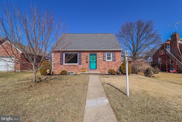 view of front facade featuring a shingled roof, a front yard, and brick siding