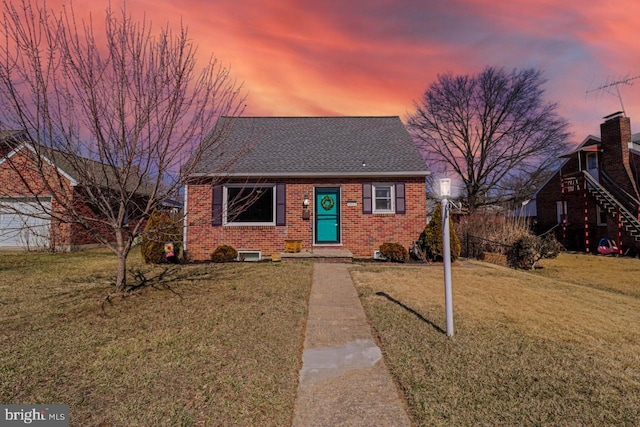 bungalow-style home with a yard, a shingled roof, and brick siding