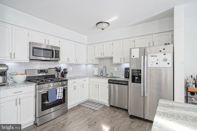 kitchen featuring stainless steel appliances, white cabinetry, a sink, and backsplash