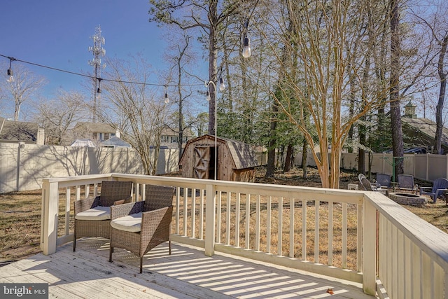 wooden terrace featuring an outdoor fire pit, a storage unit, a fenced backyard, and an outbuilding