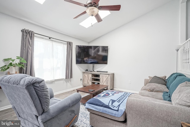 living area featuring ceiling fan, lofted ceiling with skylight, wood finished floors, and baseboards