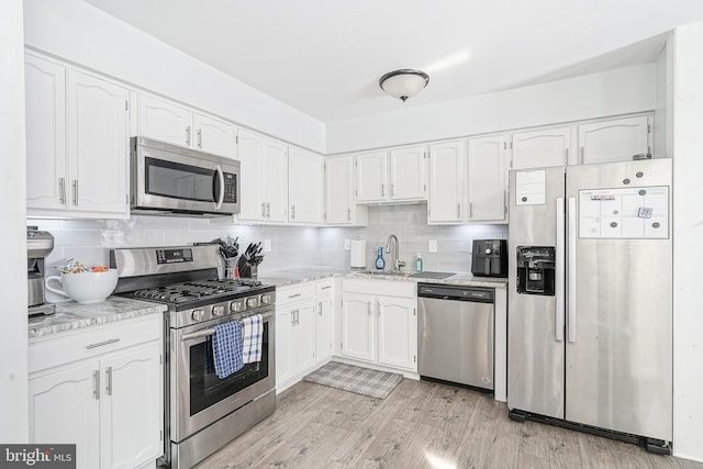 kitchen with backsplash, light wood-style flooring, appliances with stainless steel finishes, white cabinets, and a sink