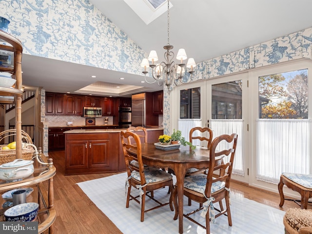 dining room with light wood finished floors, lofted ceiling with skylight, a tray ceiling, and a chandelier