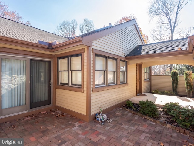 entrance to property with roof with shingles and a patio